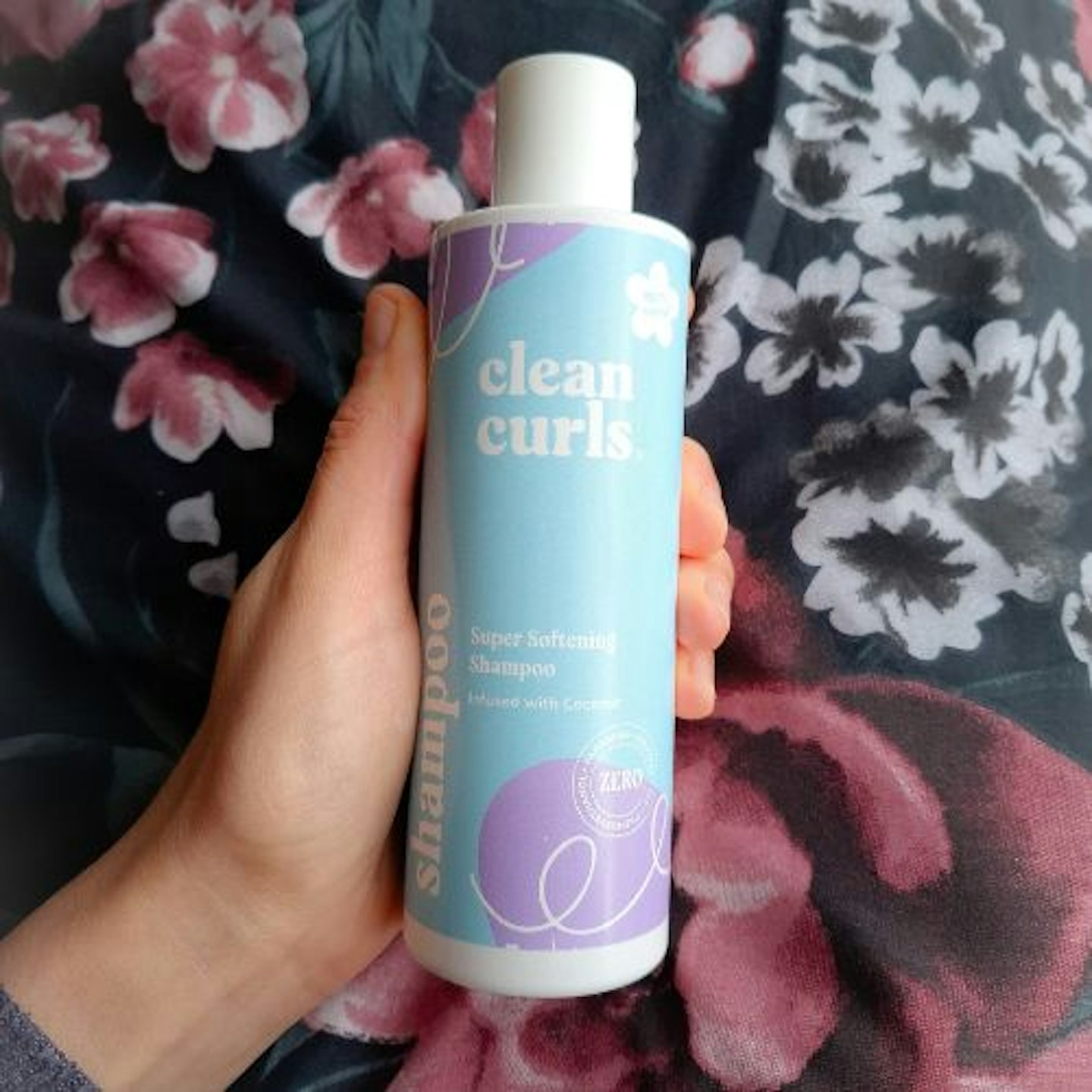 tester holding a bottle of Clean Curls Super Softening Shampoo with a flowery pattern background