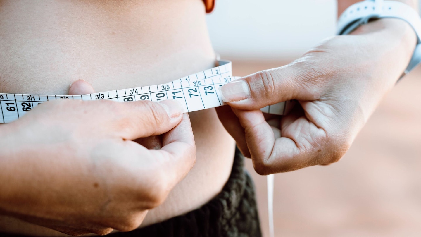 Woman measuring her waist with a tape measure