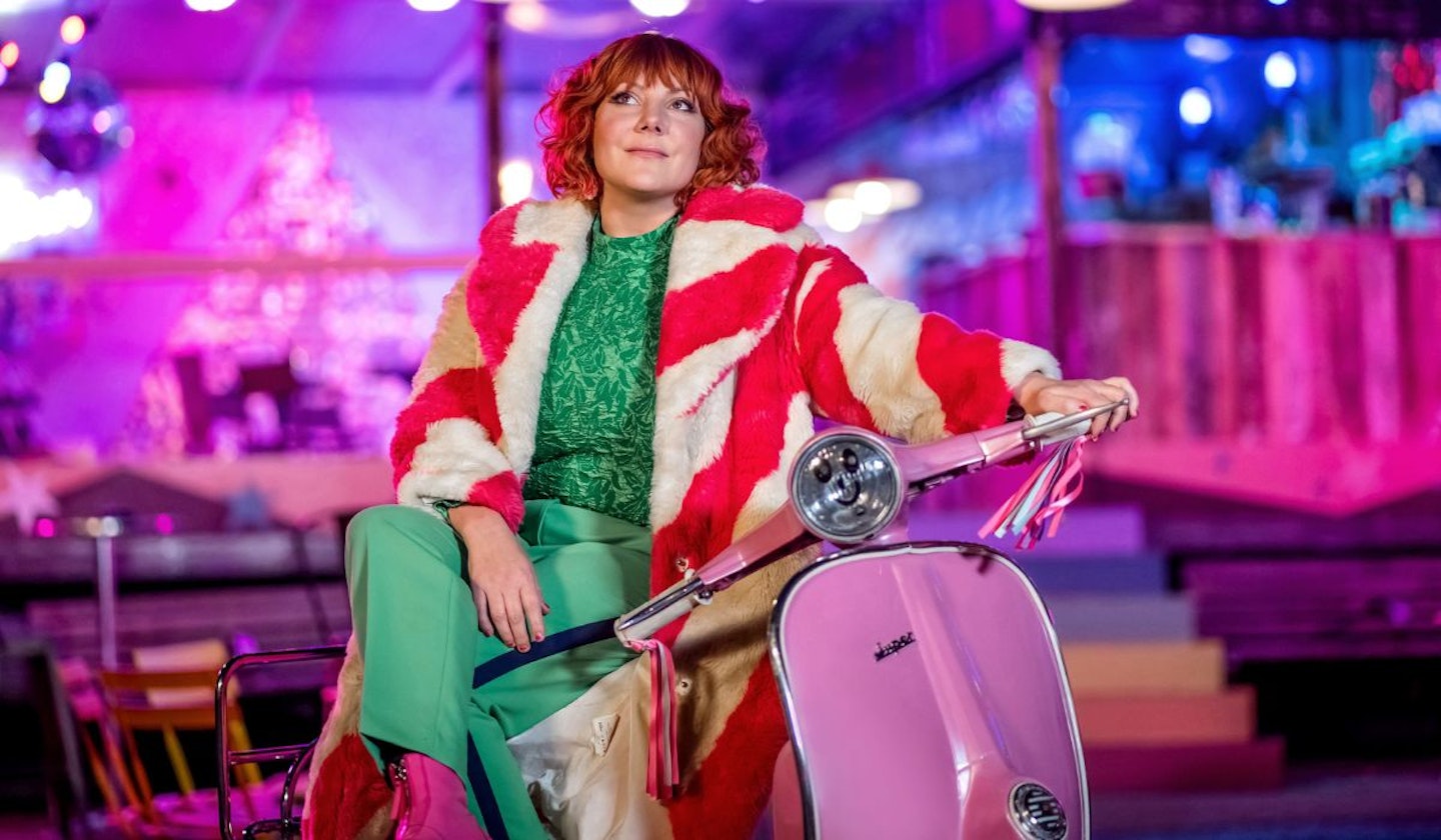 Alma (Sophie Willan) sat on a pink moped