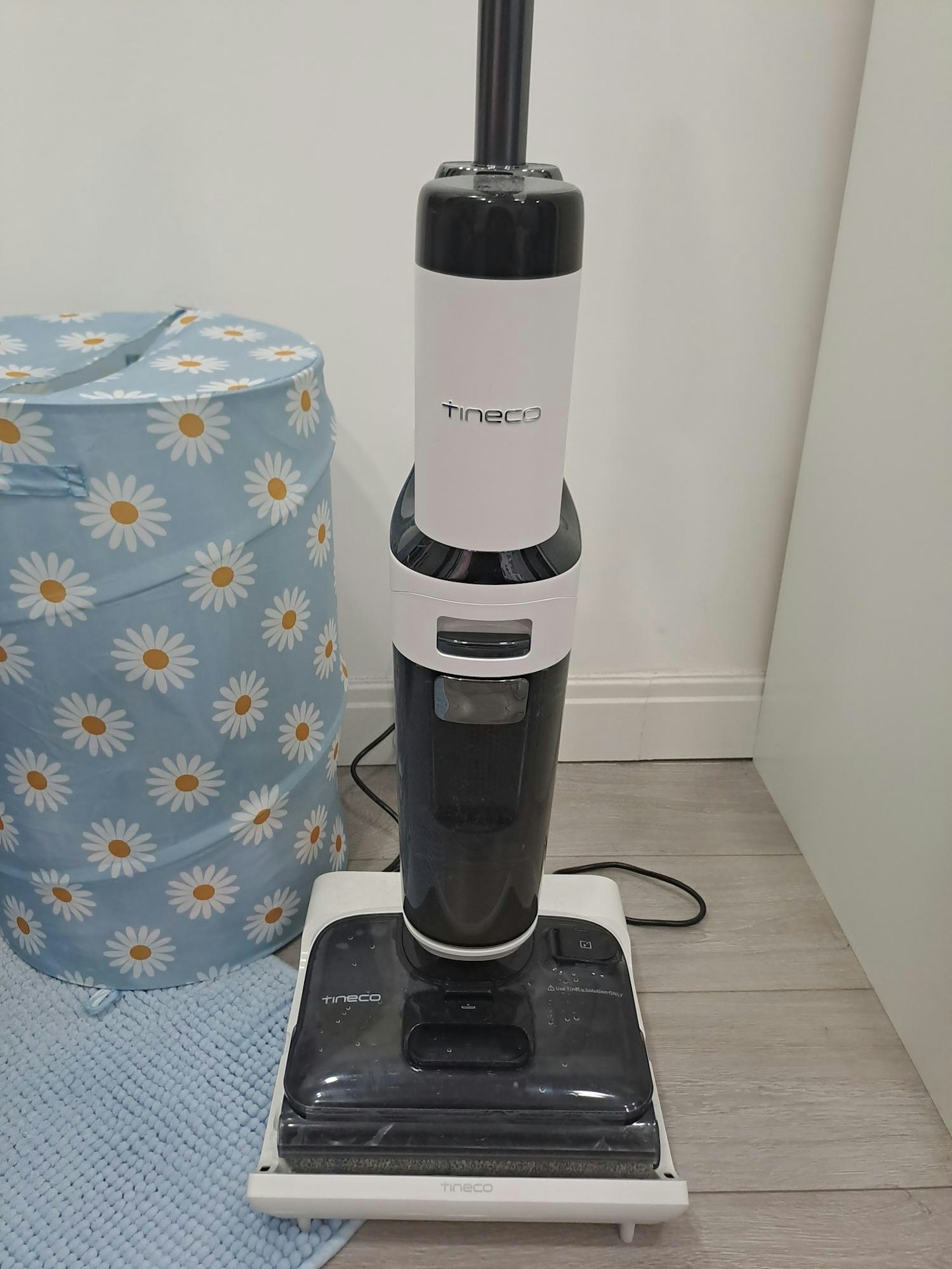 photo of the Tineco Floor ONE STRETCH S6 Cordless Wet Dry Vacuum Cleaner in a home environment next to a flower patterned laundry basket and a blue bath mat
