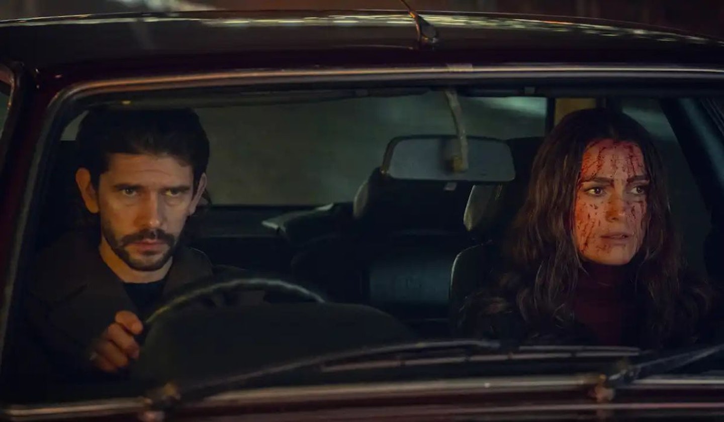 Black Doves Sam (Ben Whishaw) and Helen (Kiera Knightley) in a car look serious. Sam is driving and Helen has blood on her face.