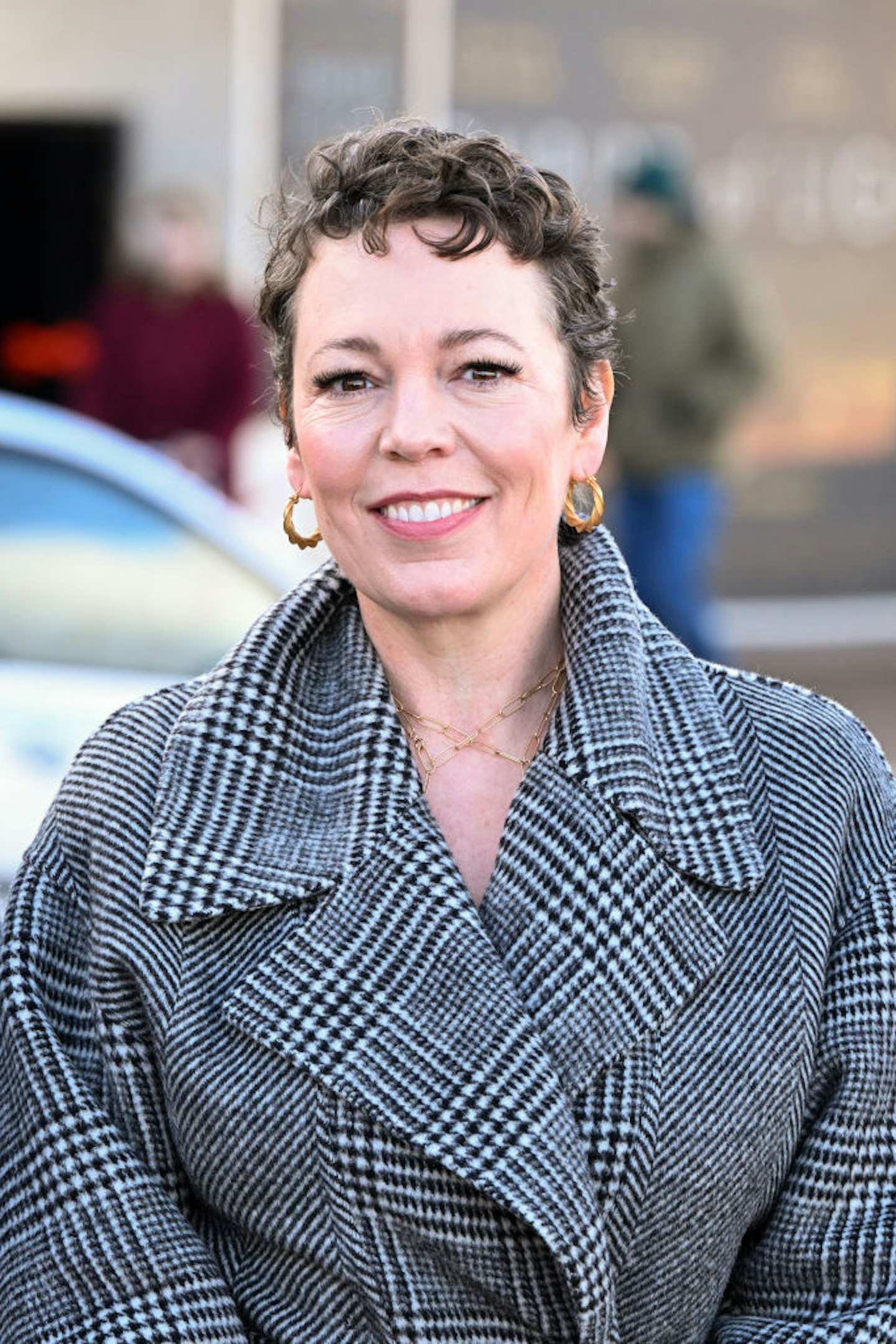 Olivia Colman in a grey and black coat with a pixie haircut