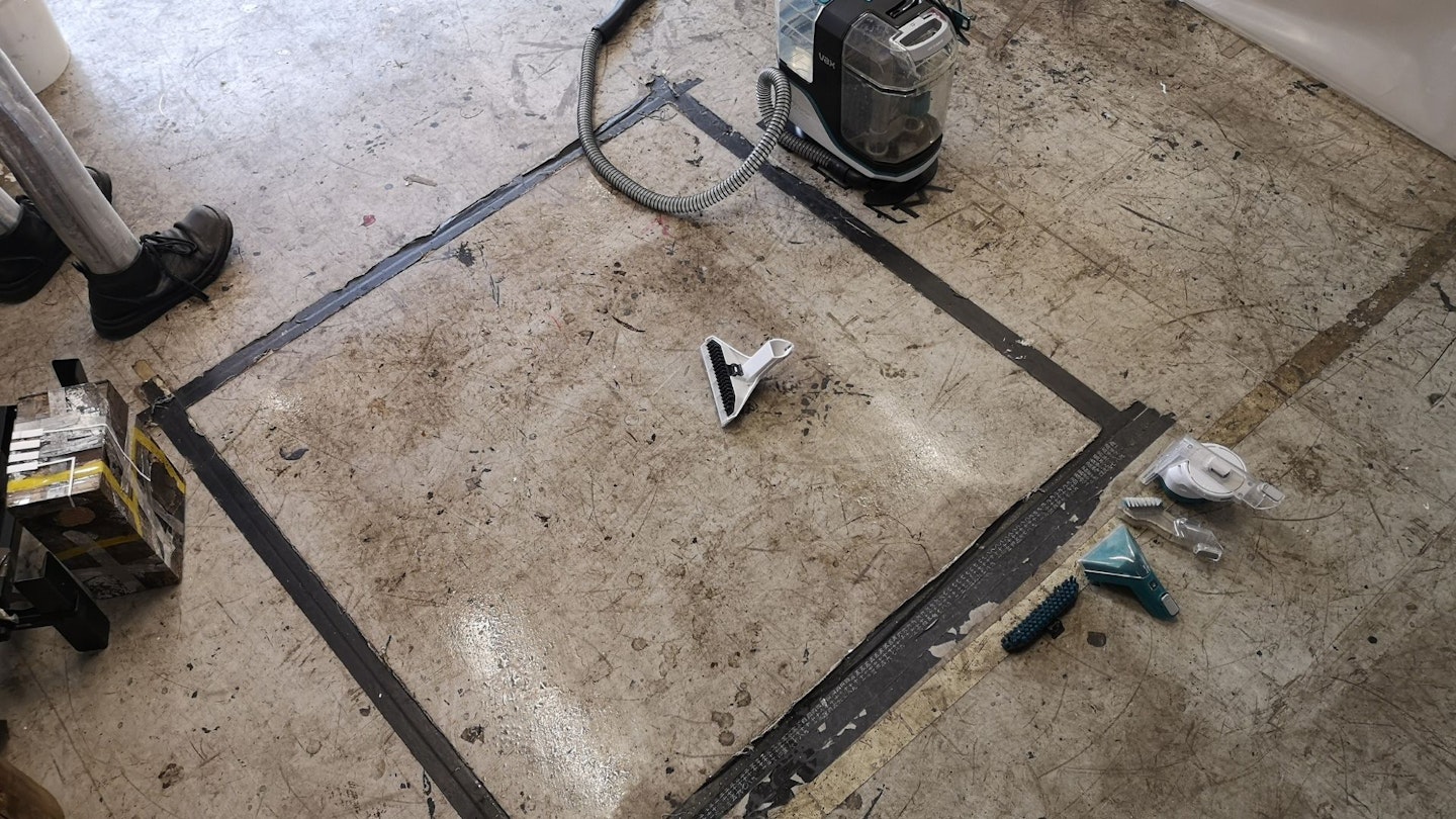 A dirty art studio floor taped off as a black square, before cleaning with a Vax SpotWash spot cleaner