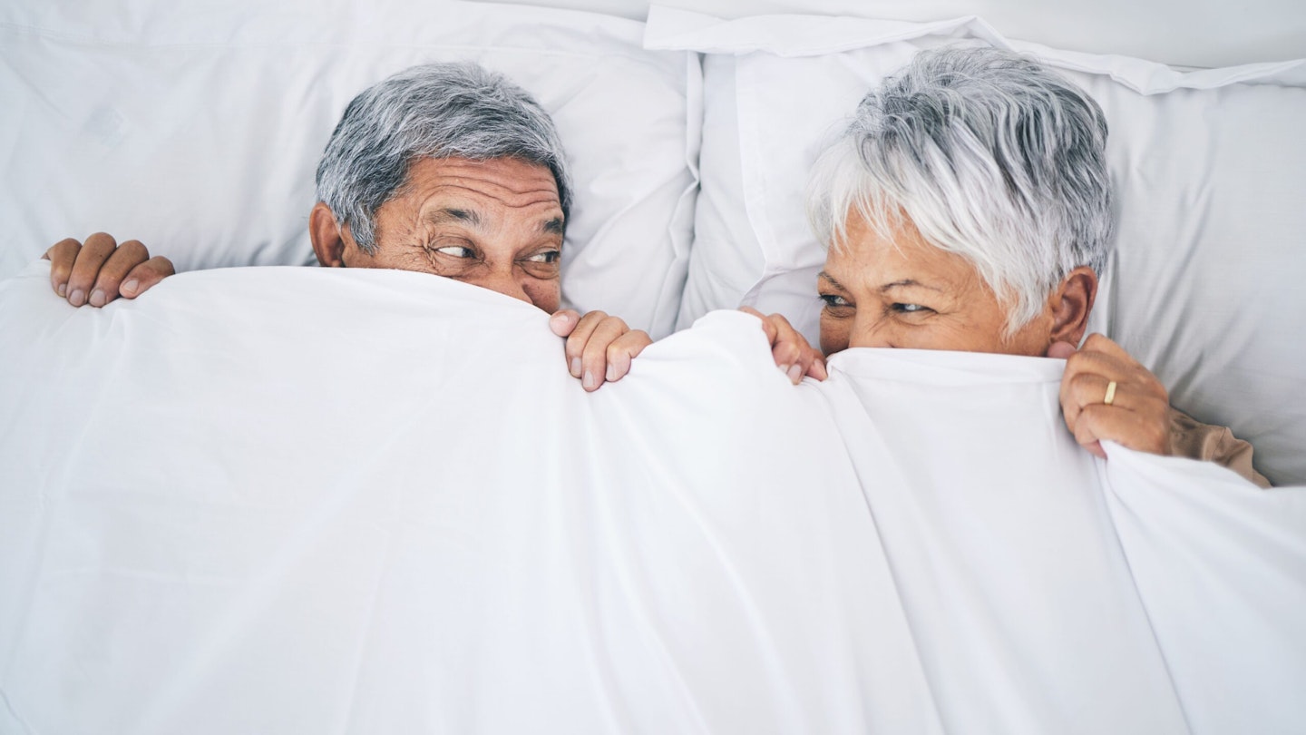 Male and female couple in bed hiding under a duvet