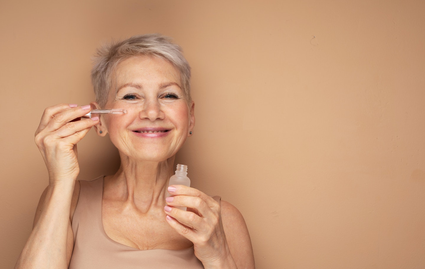 Happy senior lady applying a face oil