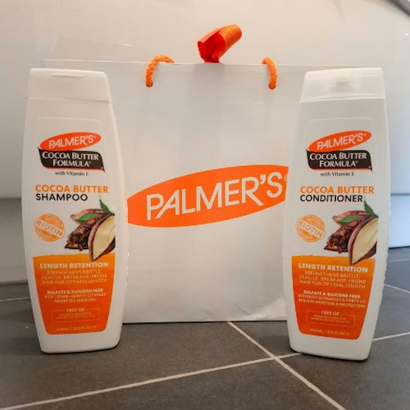 Palmers Cocoa Butter Formula Length Retention Shampoo and Conditioner in front of a branded Palmer's bag