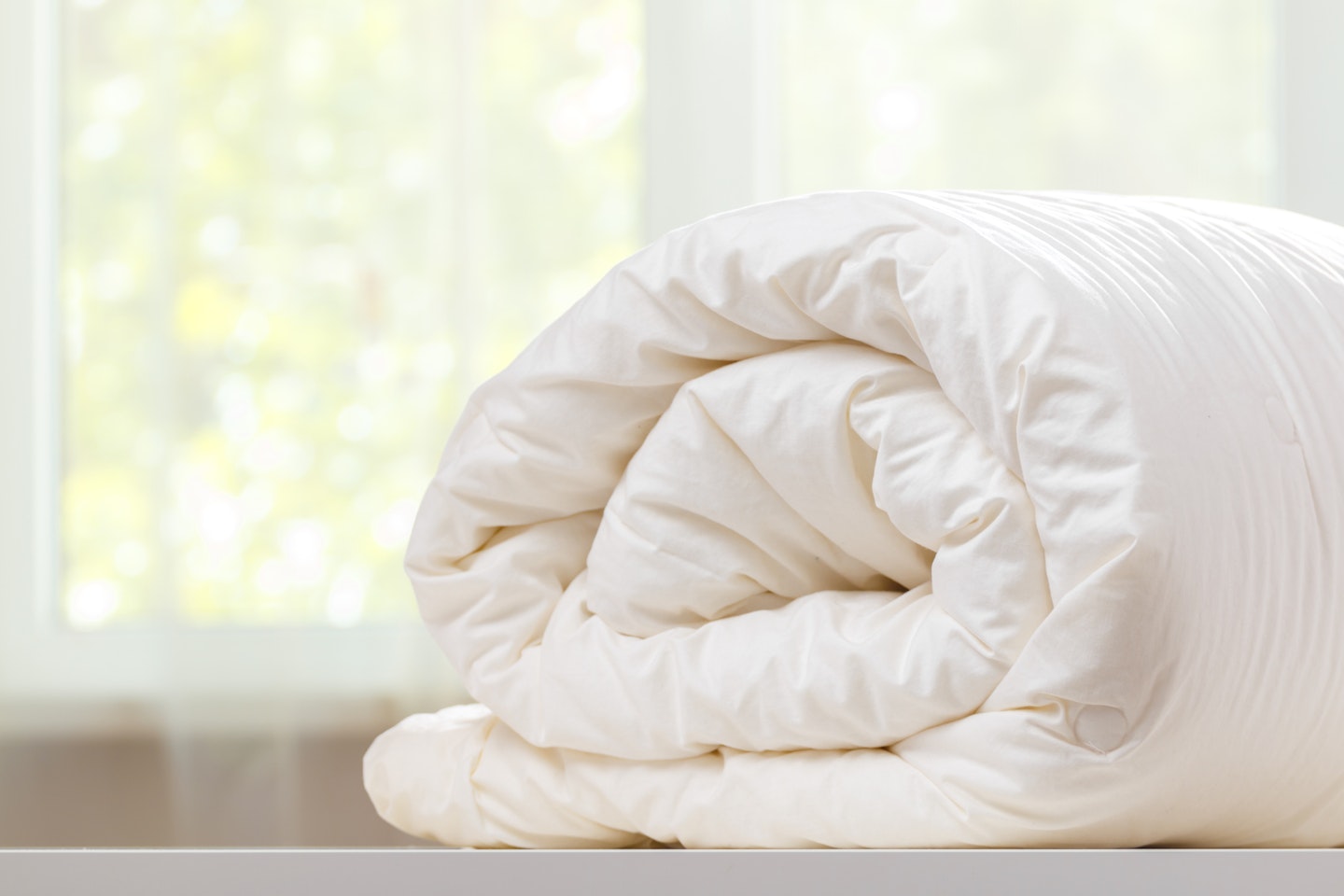 A washed duvet rolled and kept against the background of a blurred window