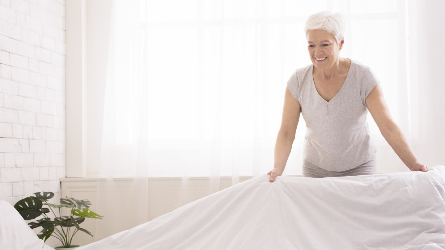 Senior woman removing the duvet from her bed