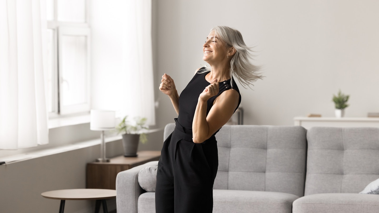 Carefree Mature blonde woman at home listening to music and dancing