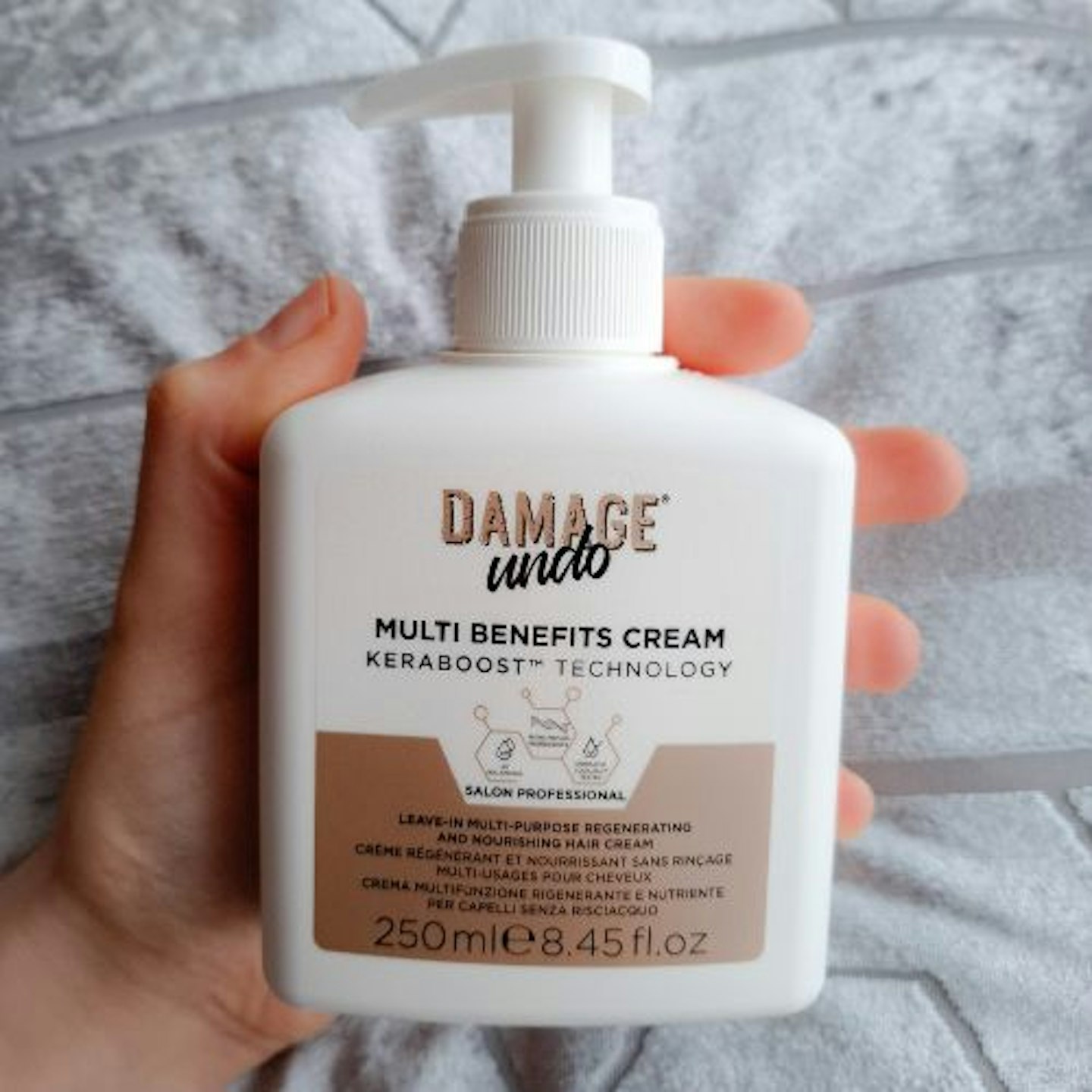 bottle of Damage Undo Multi Benefits Leave-In Cream in tester's hand, silver velvet fabric background