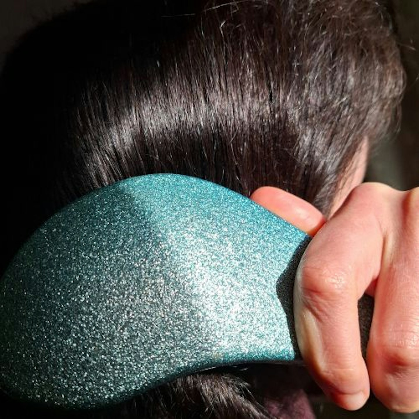 tester using a glittery turquiose hairbrush on her dark brown hair