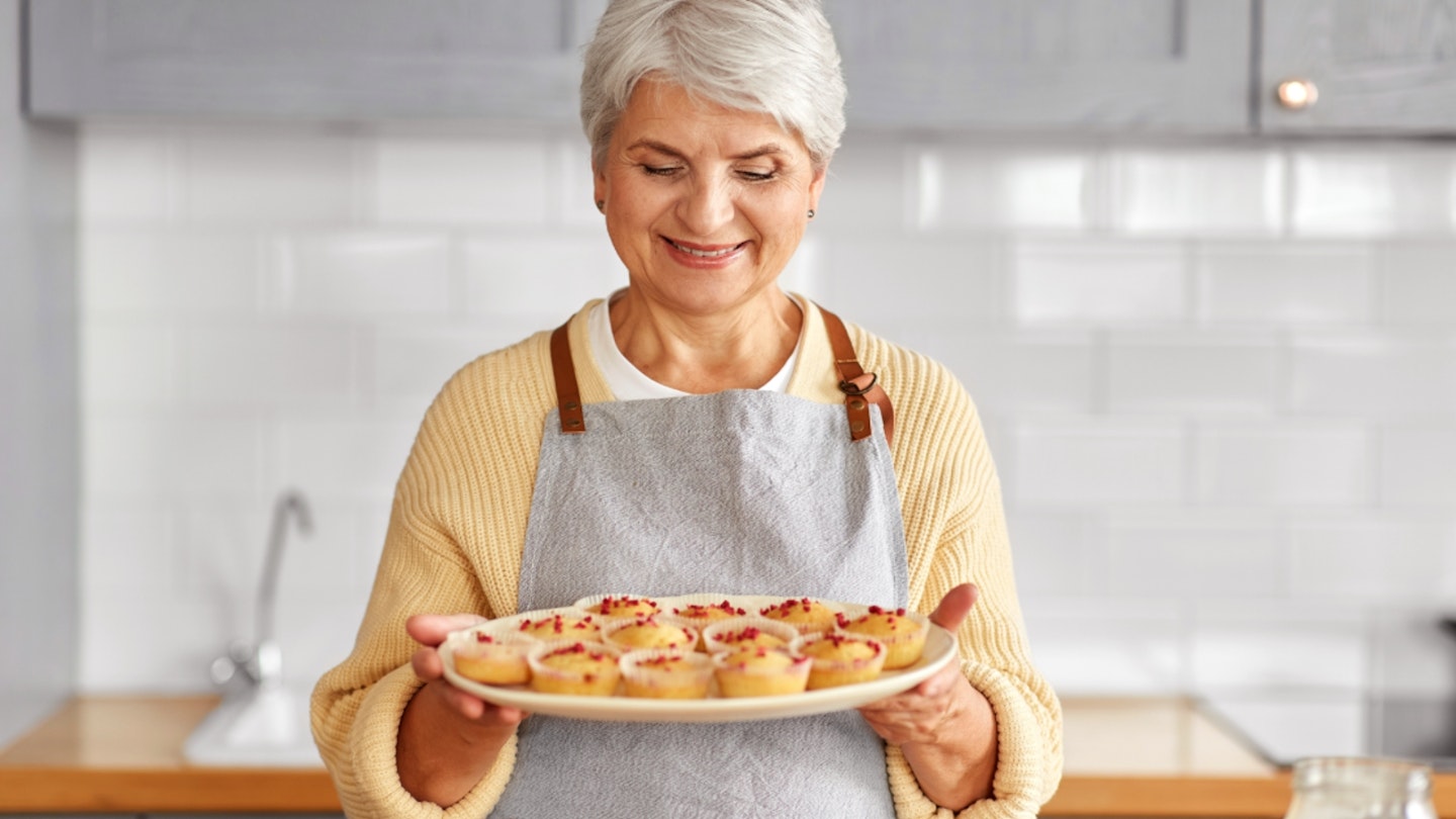 Happy senior woman holding big plate of cupcakes