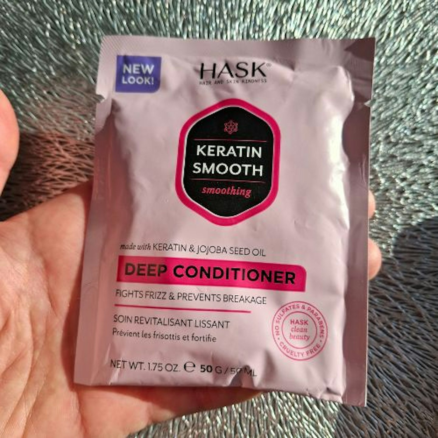 sachet of Hask Keratin Smooth Deep Conditioner in tester's hand, silver grain background