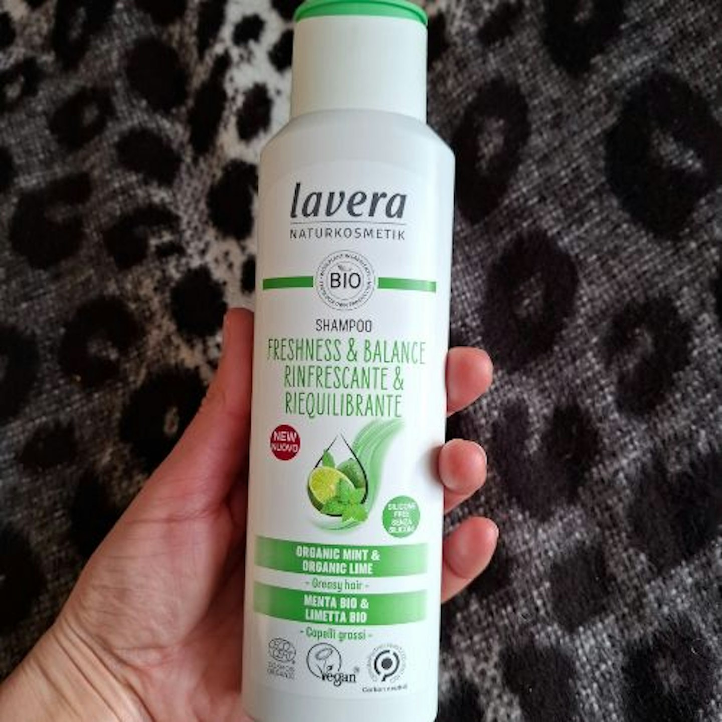 bottle of Lavera Freshness and Balance Shampoo in tester's hand, black and white leopard print material background