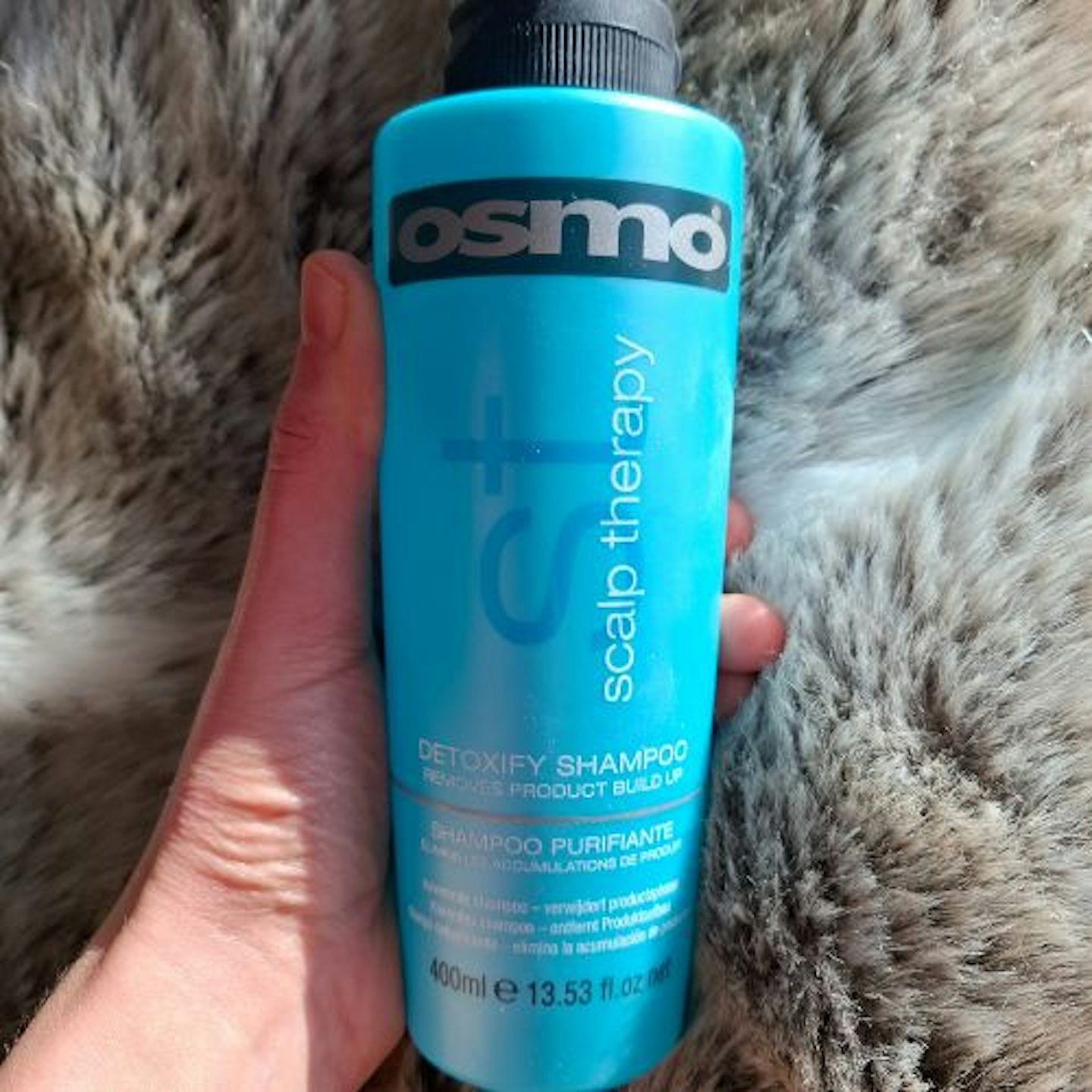 tester' holding a bottle of OSMO Scalp Therapy Detoxifying Shampoo, faux fur background