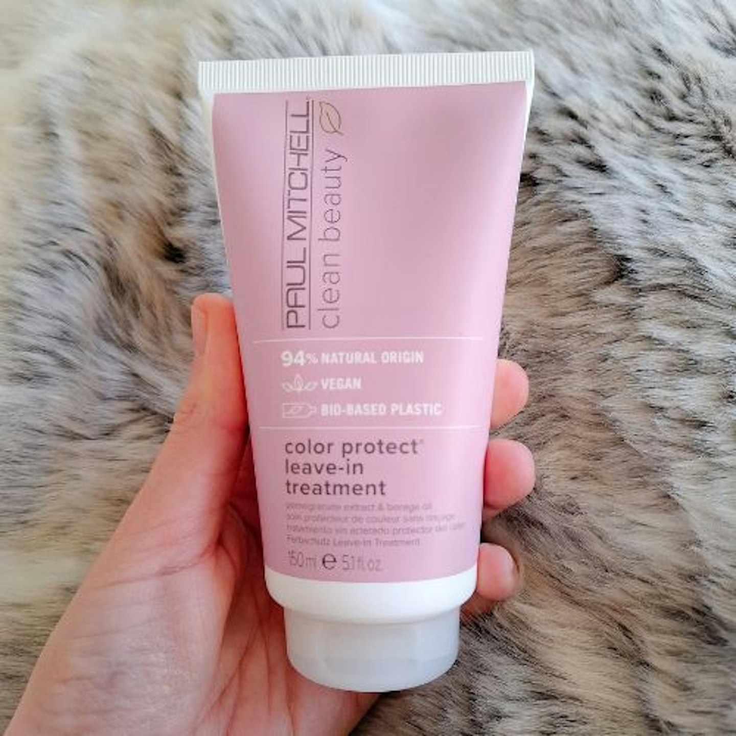 tube of Paul Mitchell Clean Beauty Color Protect Leave-In Treatment in tester's hand on a faux fur background