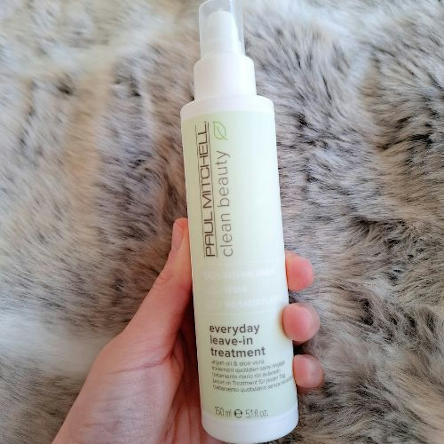 bottles of Paul Mitchell Clean Beauty Everyday Leave-In Treatment in tester's hand on faux fur background