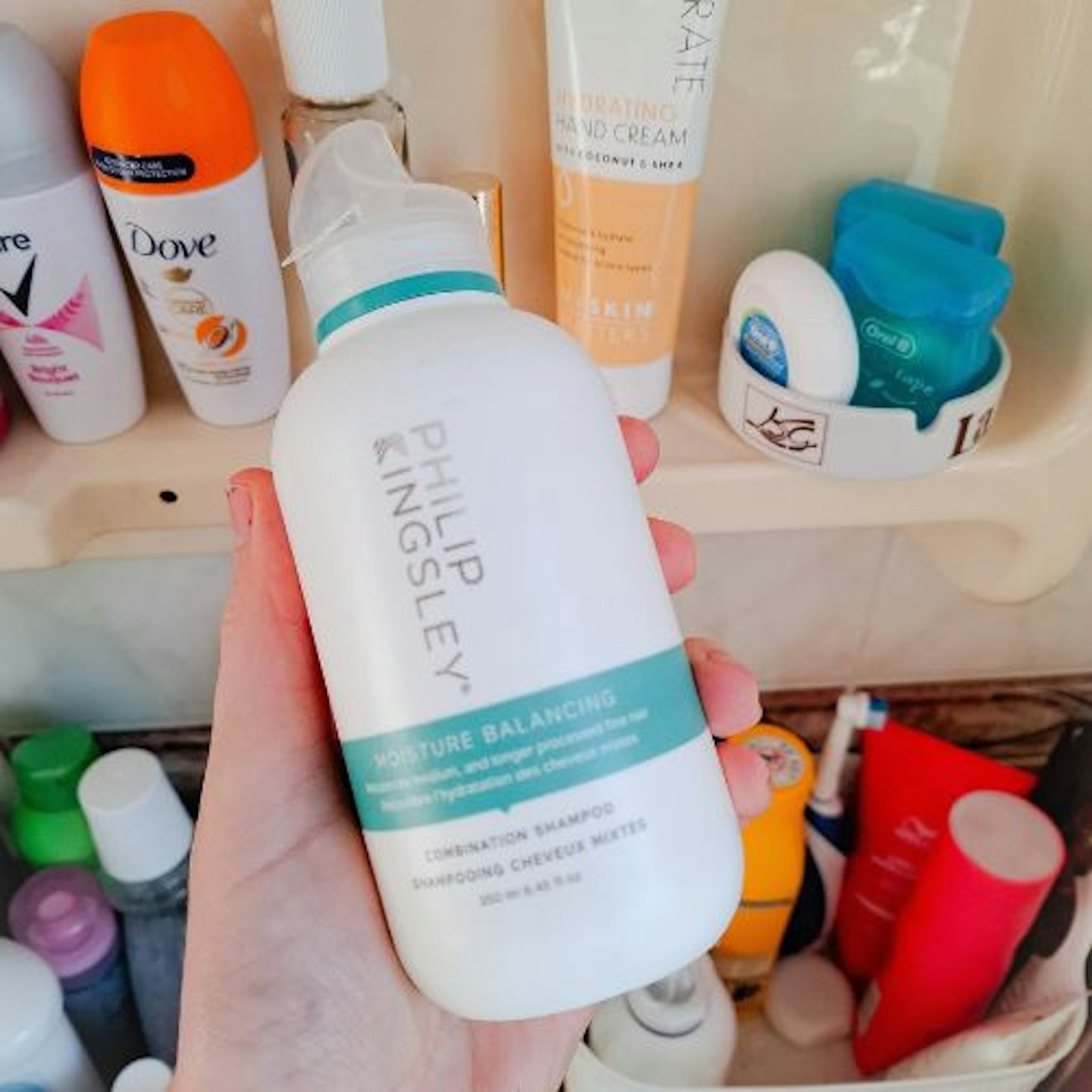 Philip Kingsley’s Moisture Balancing Shampoo bottle in tester's hand with other beauty products on shelves behind