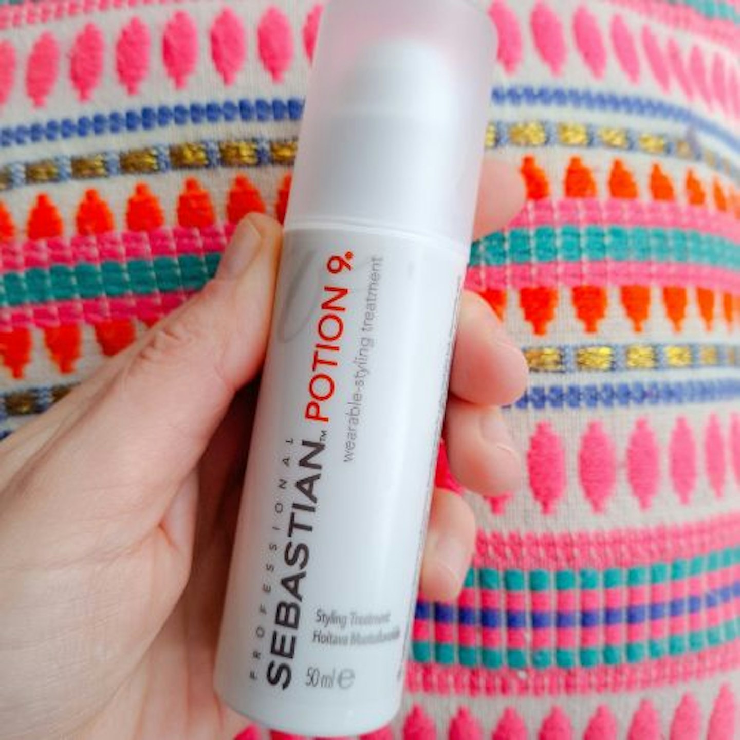 tube of Sebastian Professional Potion 9 Leave-In Styling Conditioner in tester's hand on a bright neon patterned cushion