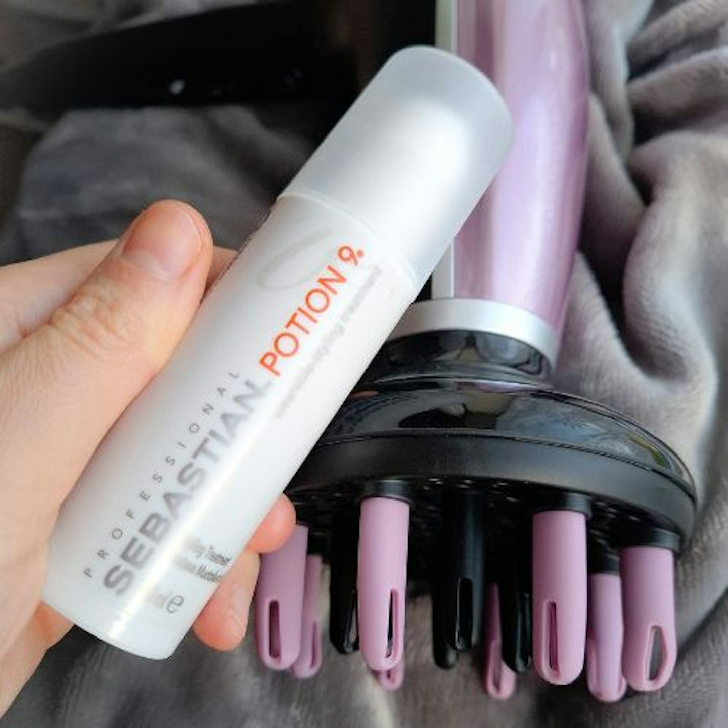 tester's hand holding a tube of Sebastian Professional Styling Conditioner next to a purple hair dryer with a diffuser