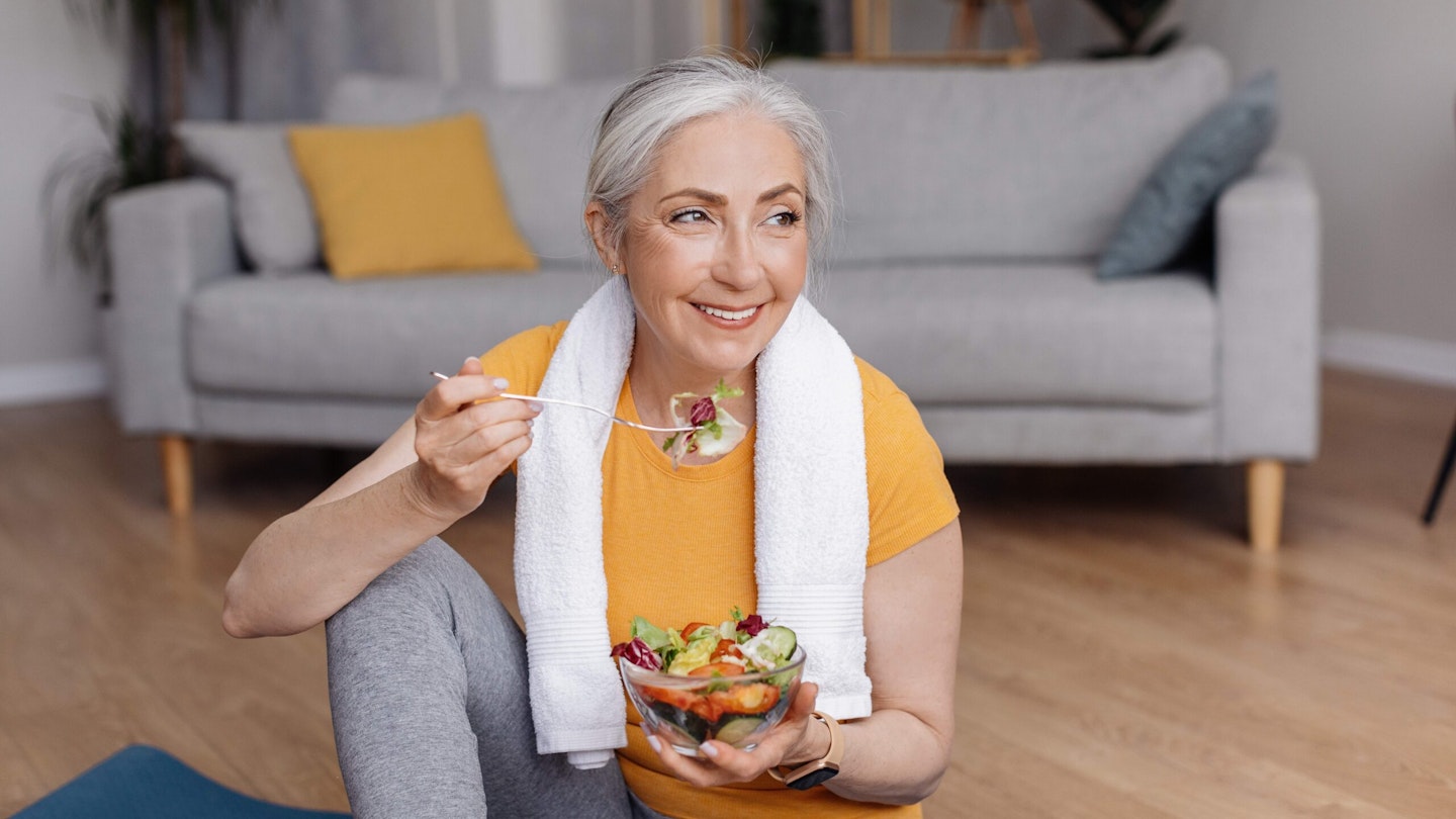 Woman in yellow t-shirt with towel over her shoulder, eating a salad