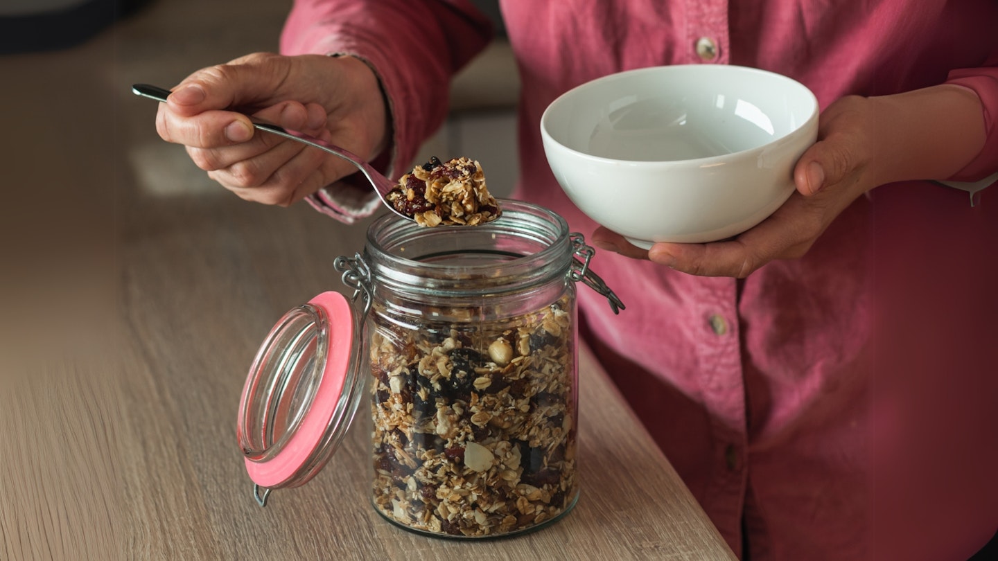 A mature woman puts homemade granola or muesli from a jar in a bowl.