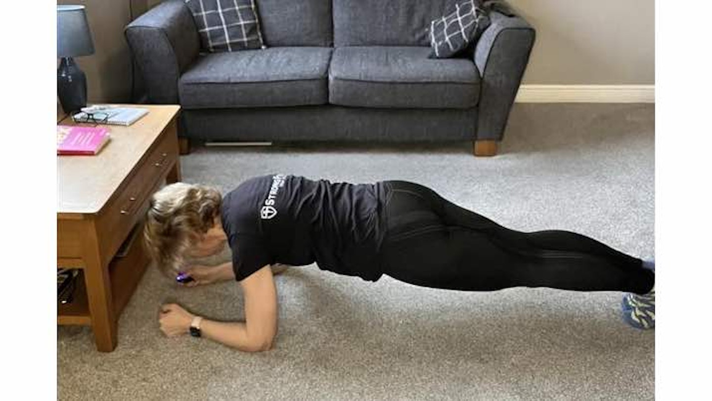 Woman doing a plank at home on a grey carpet