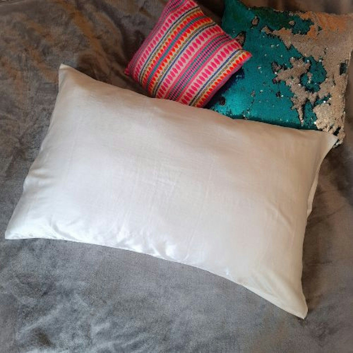 photo of Only Curls Silk Pillowcase on a pillow with two brightly coloured cushions beside it, on a silver fleece throw 