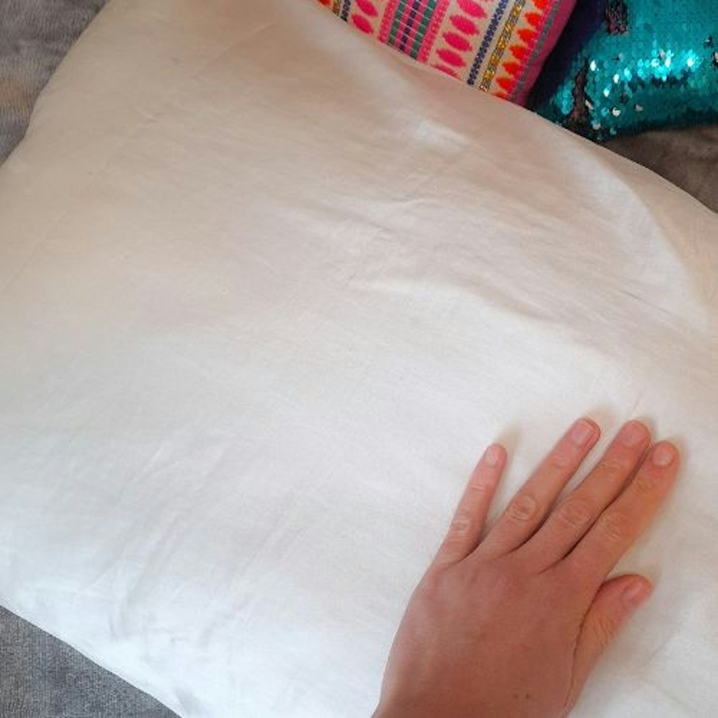 tester's hand smoothing over the surface of an Only Curls Silk Pillowcase, with brightly coloured cushions in background