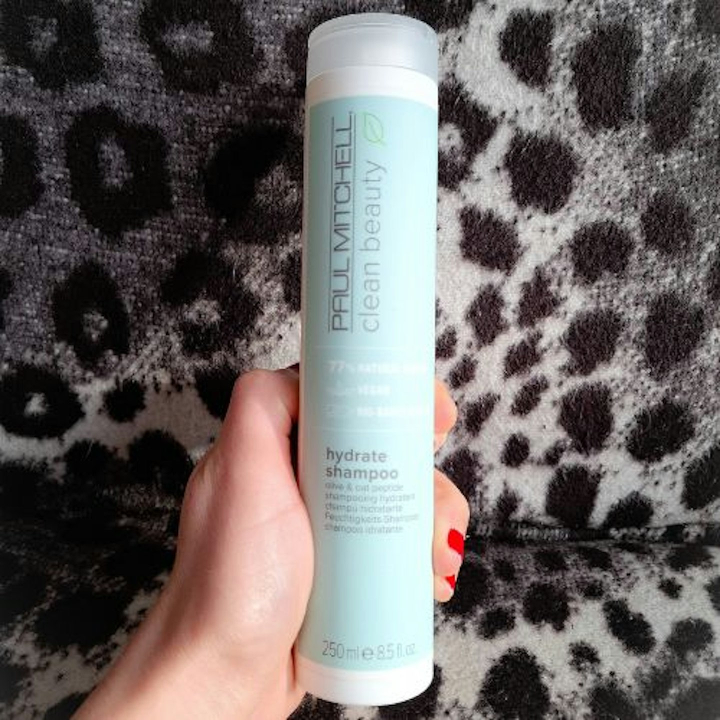 bottle of Paul Mitchell Clean Beauty Hydrate Shampoo in tester's hand, monochrome leopard print background