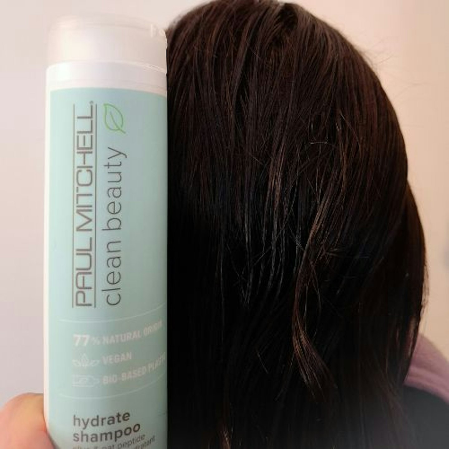 back of tester's damp, unstyled, dark brown hair and a bottle of Paul Mitchell Clean Beauty Hydrate Shampoo