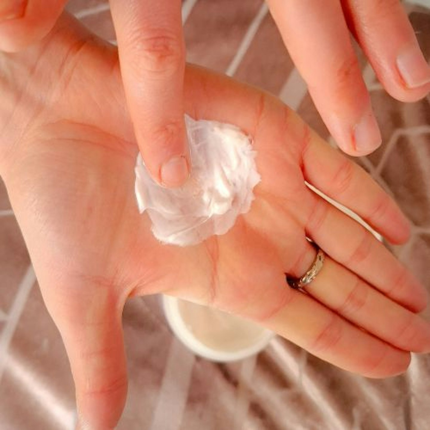 close up of tester's outstretched palm, spreading Philip Kingsley Extreme Elasticizer cream to demonstrate its thick consistency