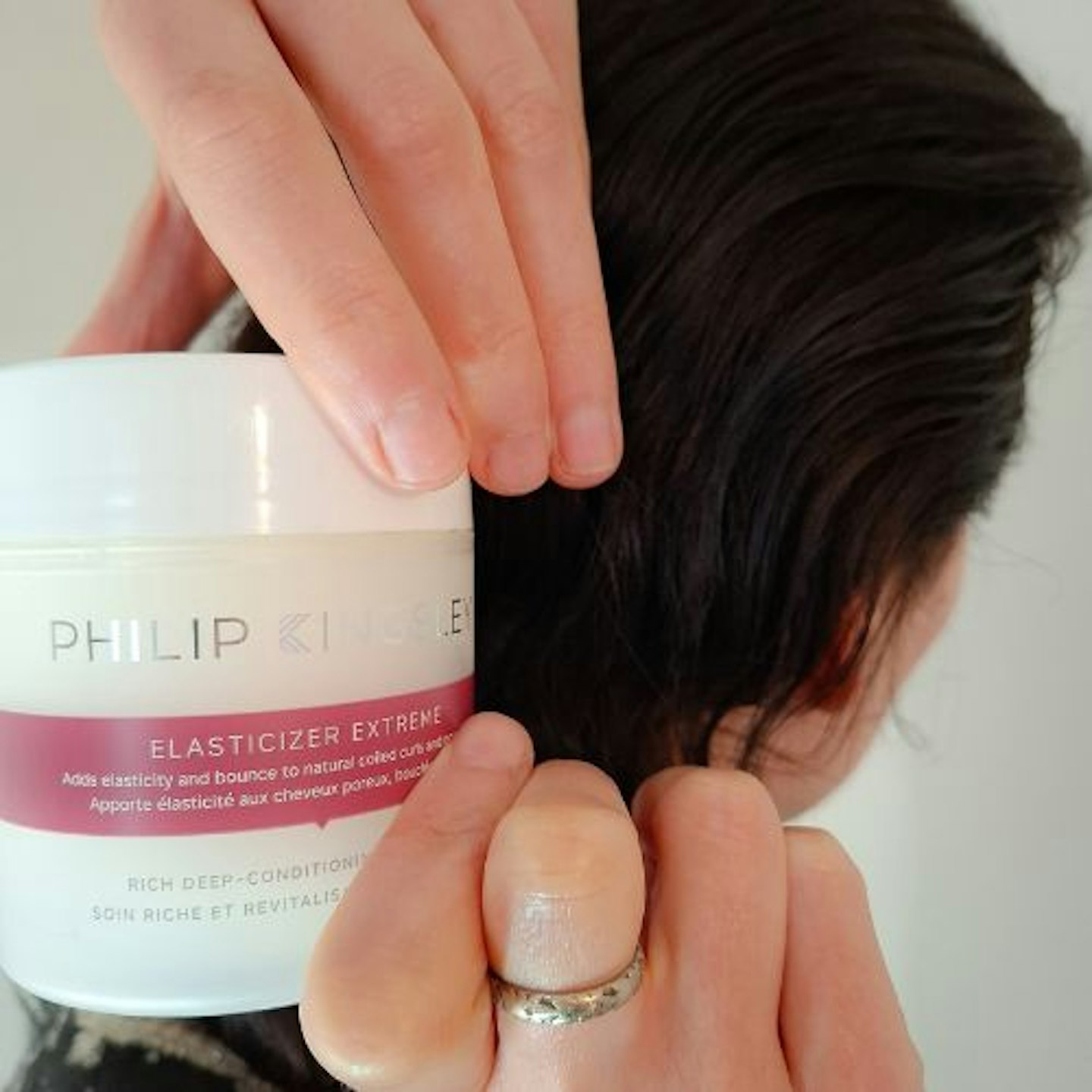 extreme close up of a pot of Philip Kingsley Extreme Elasticizer in tester's hands with a side view of her head - dark brown slicked back hair