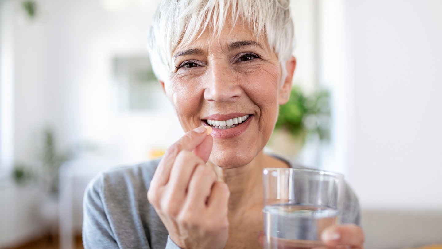 Woman holding glass of water, takeing daily vitamin D pill