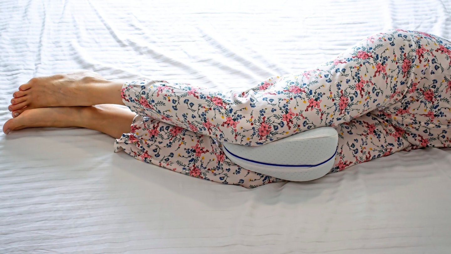 Woman with an anatomical pillow between her legs and knees, lying on a bed