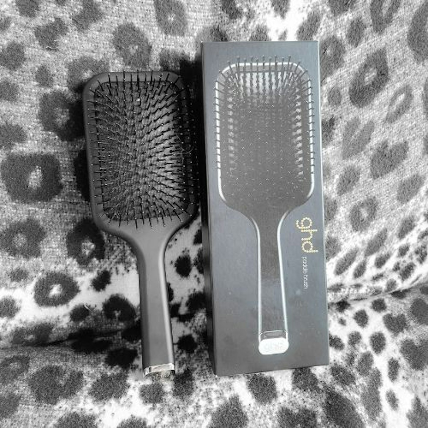 ghd paddle brush standing next to its box on a monochrome faux leopard background