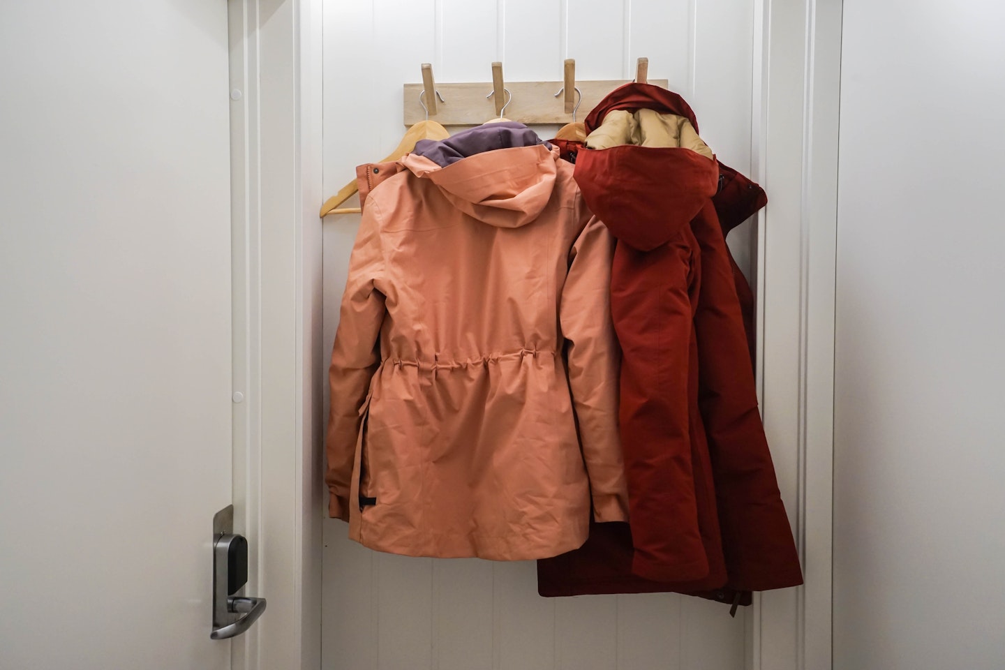 Orange and red winter jackets hang on a wall hook near the house door