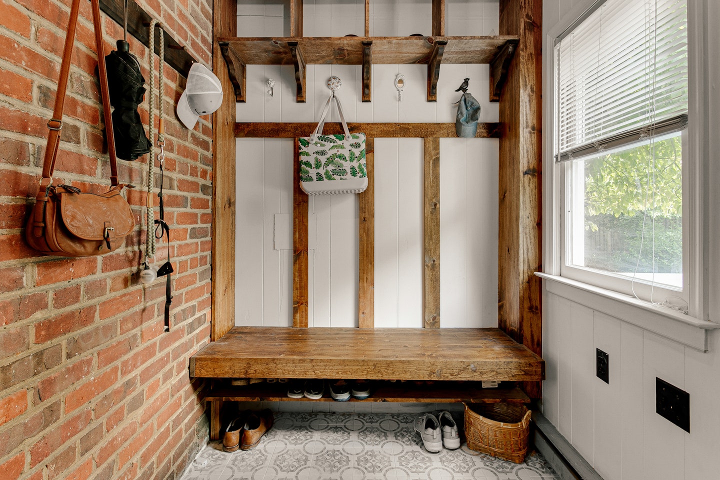 Rustic Mudroom With Brick Wall, Wooden Bench, Hooks, And Various Hanging Items.