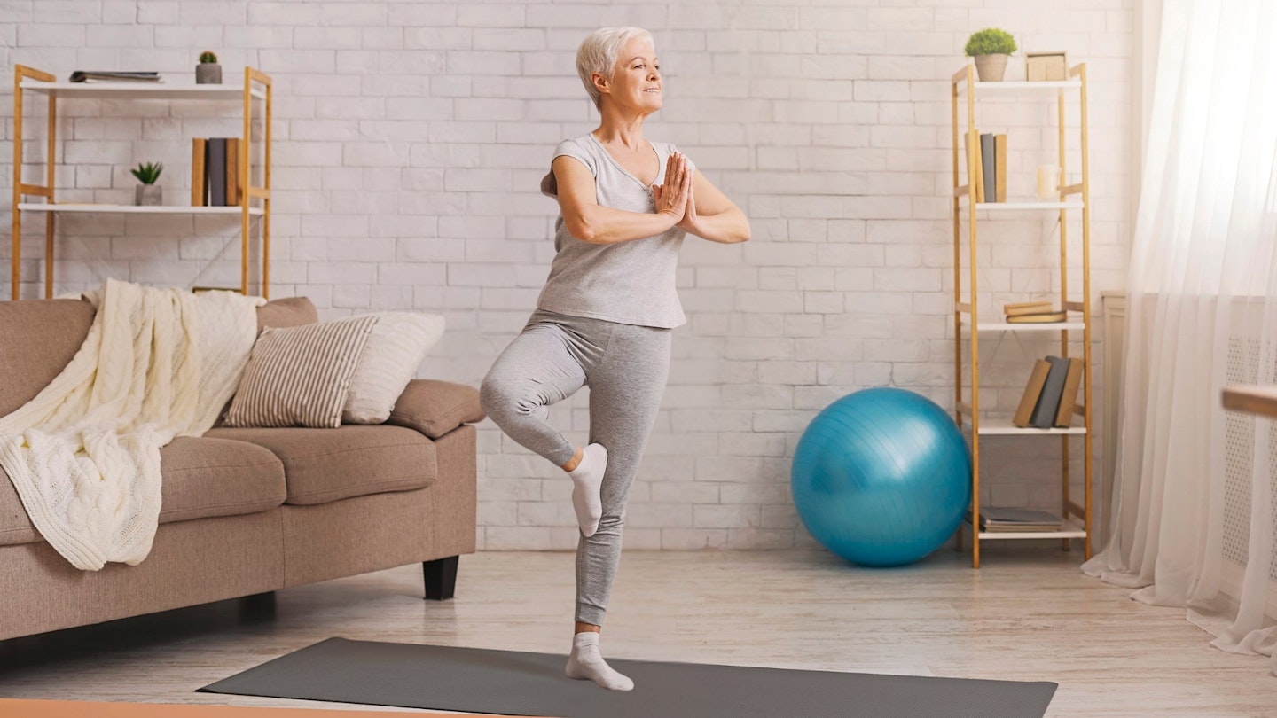 Balance in life. Senior woman doing yoga tree pose at home