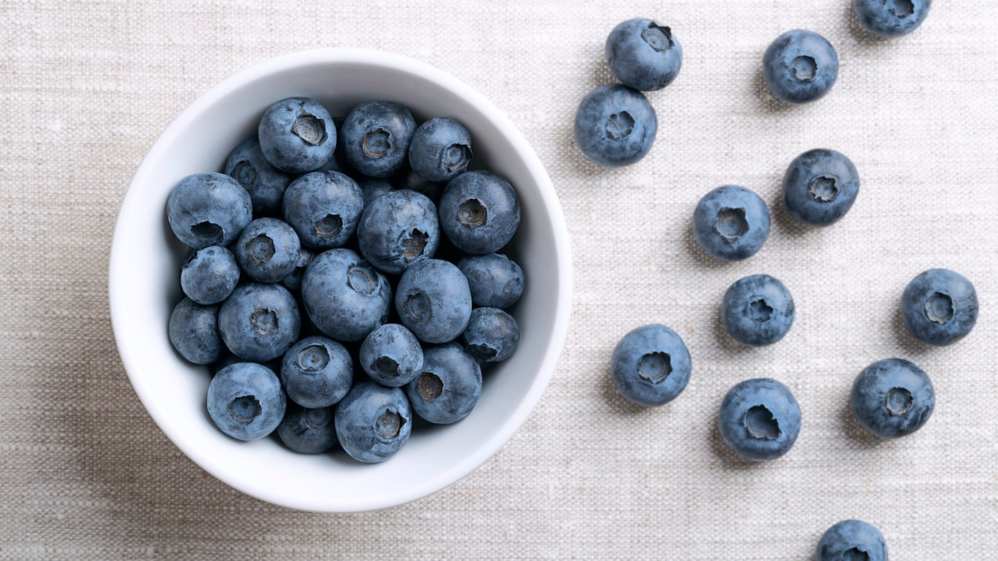 A bowl of blueberries with some scattered on the side