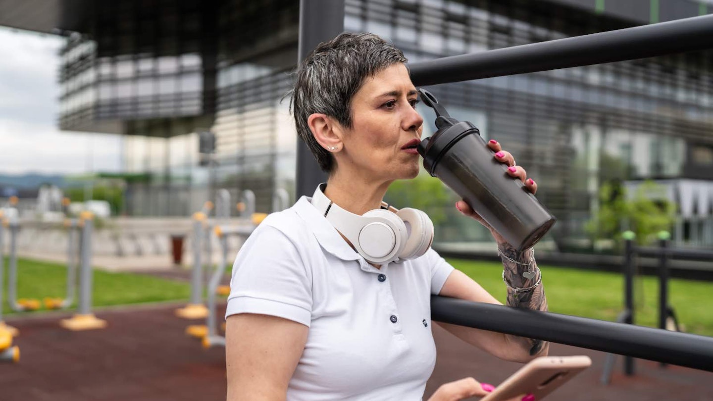 Woman on sports track, in white t-shirt, drinking a protein shake