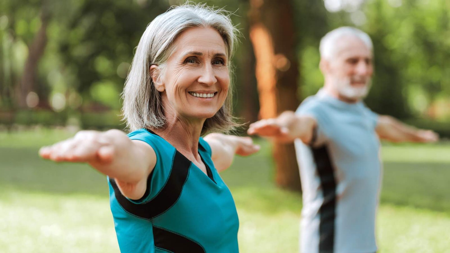 Man and woman in park staring with arms extended horizontally