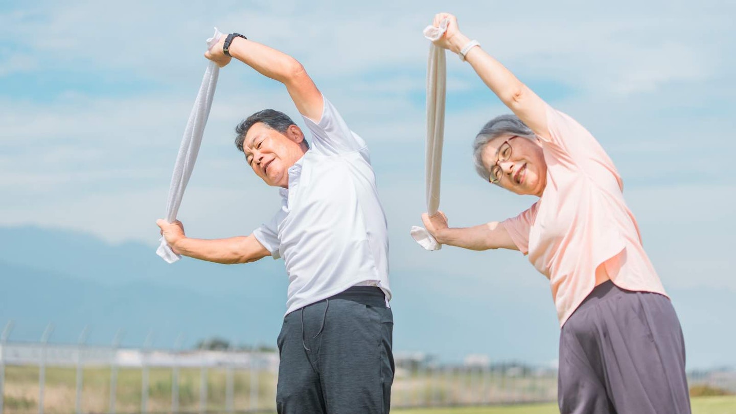 man and woman doing side bends with resistance band stretched out wide overhead