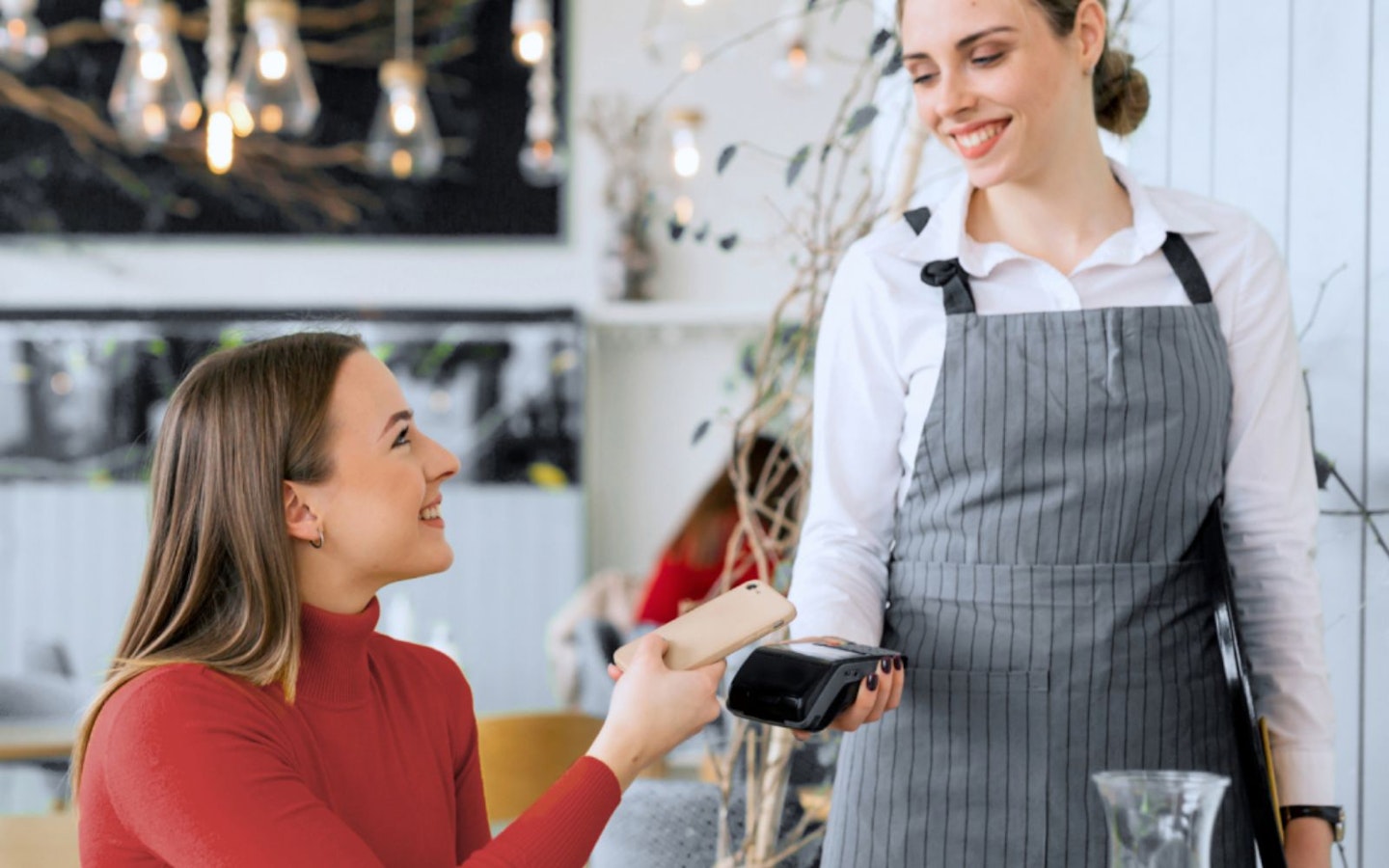 A woman paying for something in a cafe using a smartphone