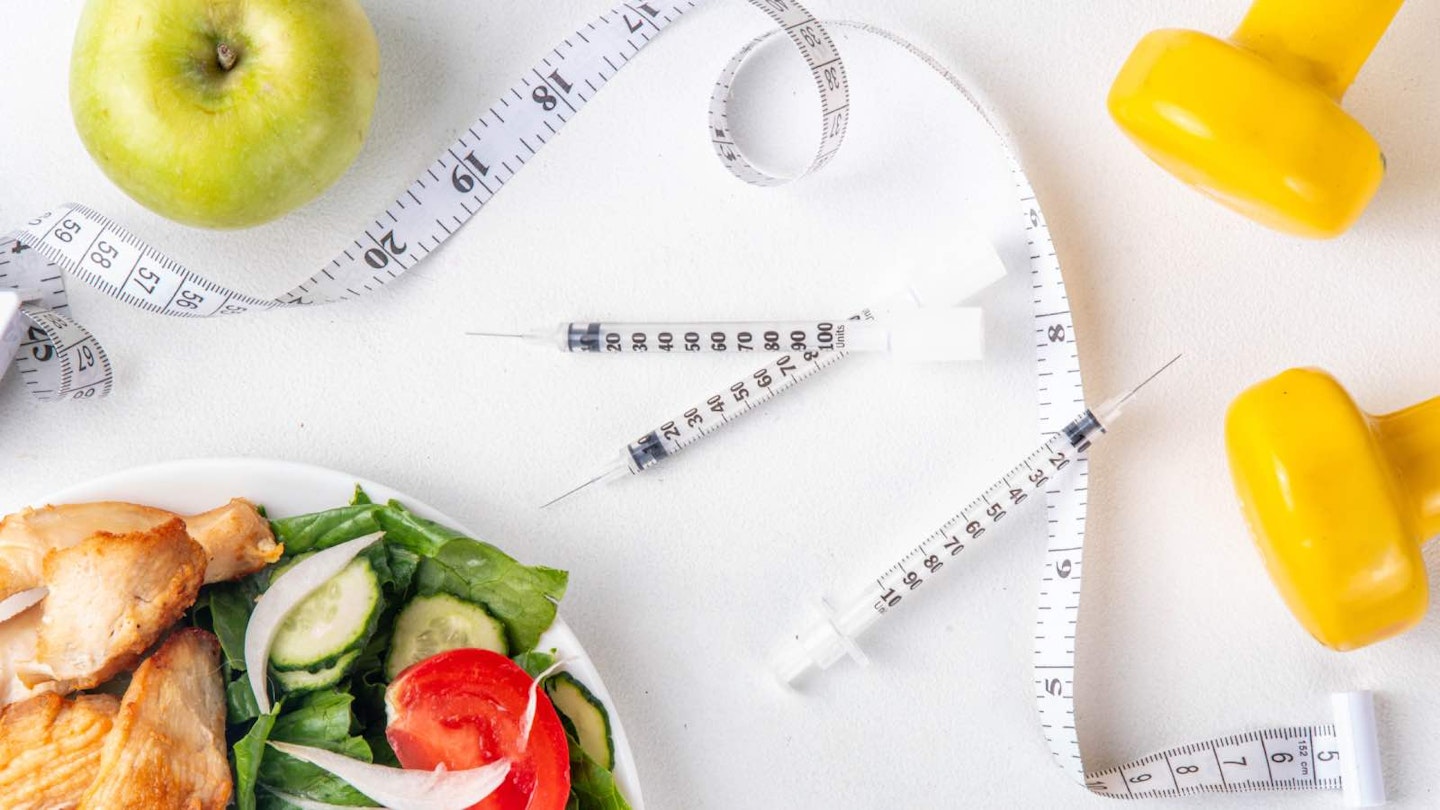 Weight loss injections, a pair of yellow dumbbells, a tape measure, an apple and a bowl of chicken salad