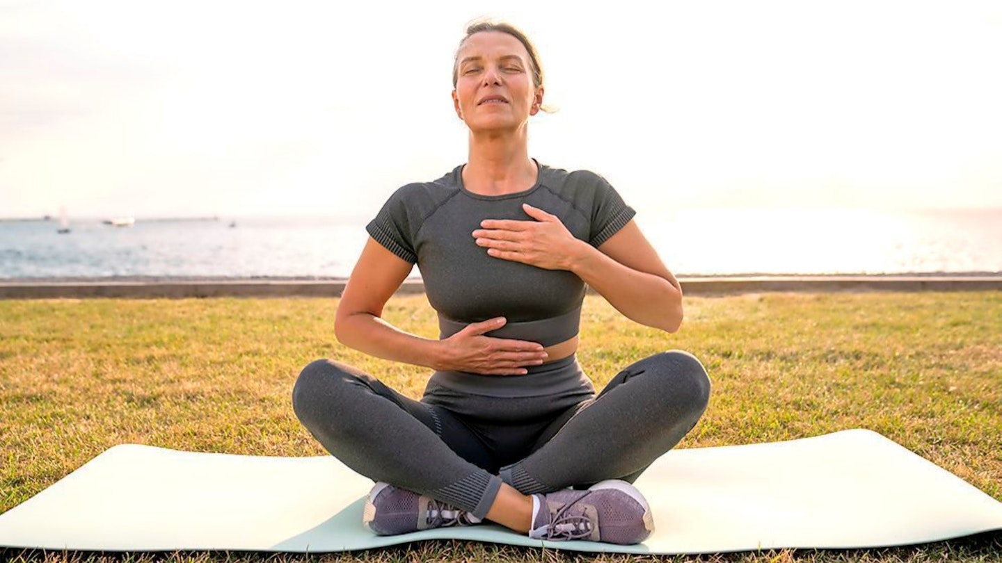 Lady sitting on mat out door doing breathing exercises