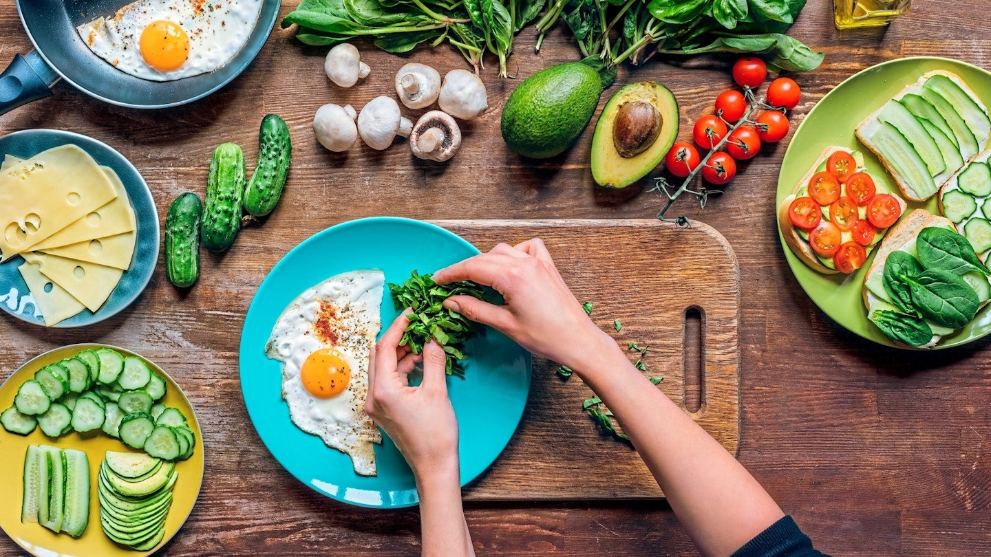 Hand making meal on a plate surrounded by fresh vegetables