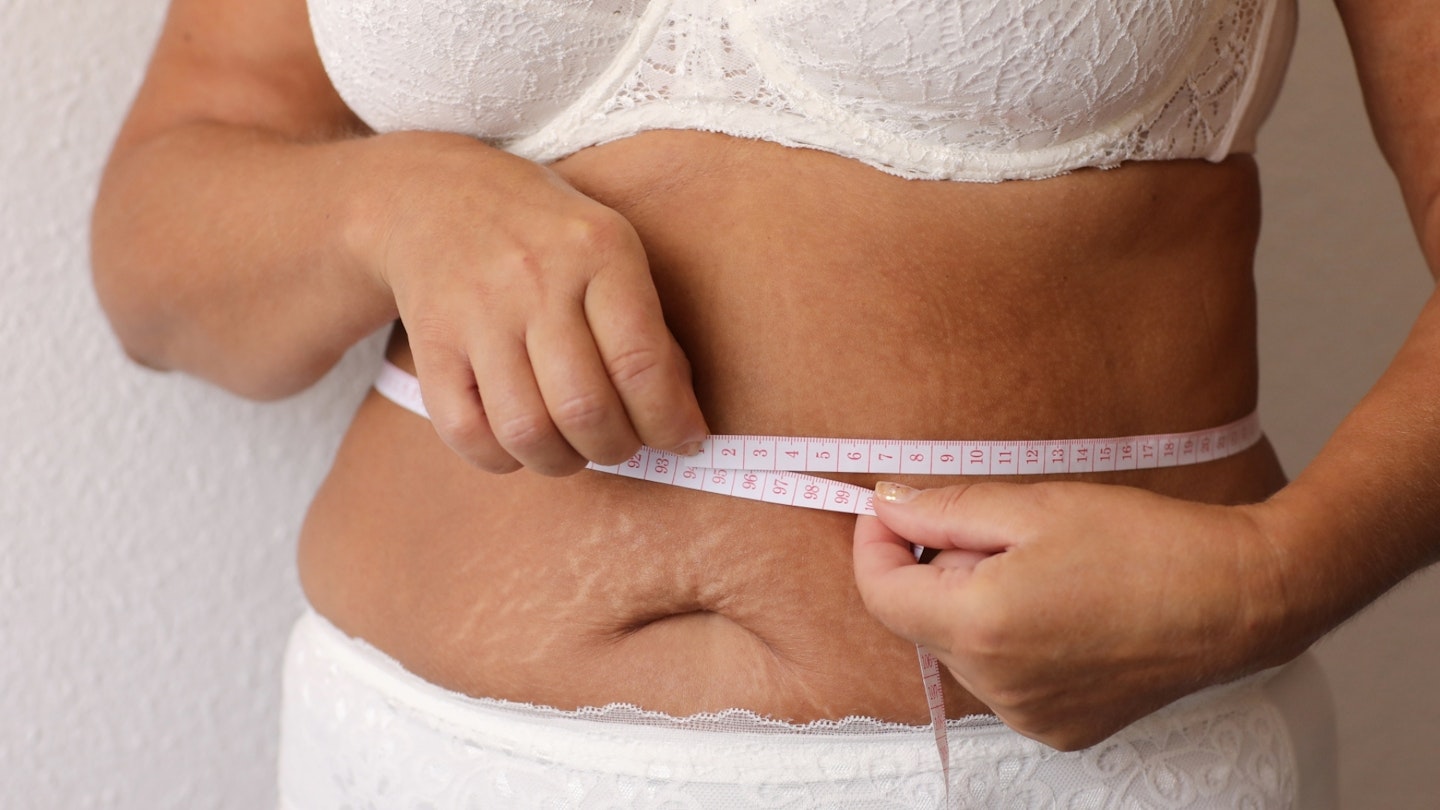 Woman measuring her waist with tape measure