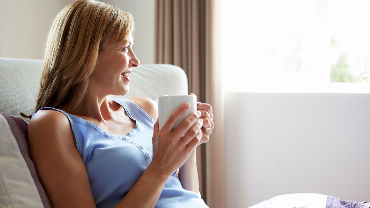 Smiling woman drinking a cup of tea looking out the window