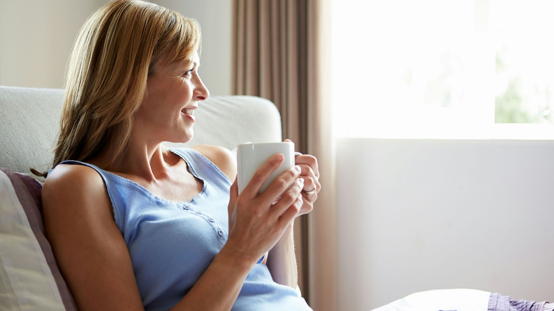 Smiling woman drinking a cup of tea looking out the window